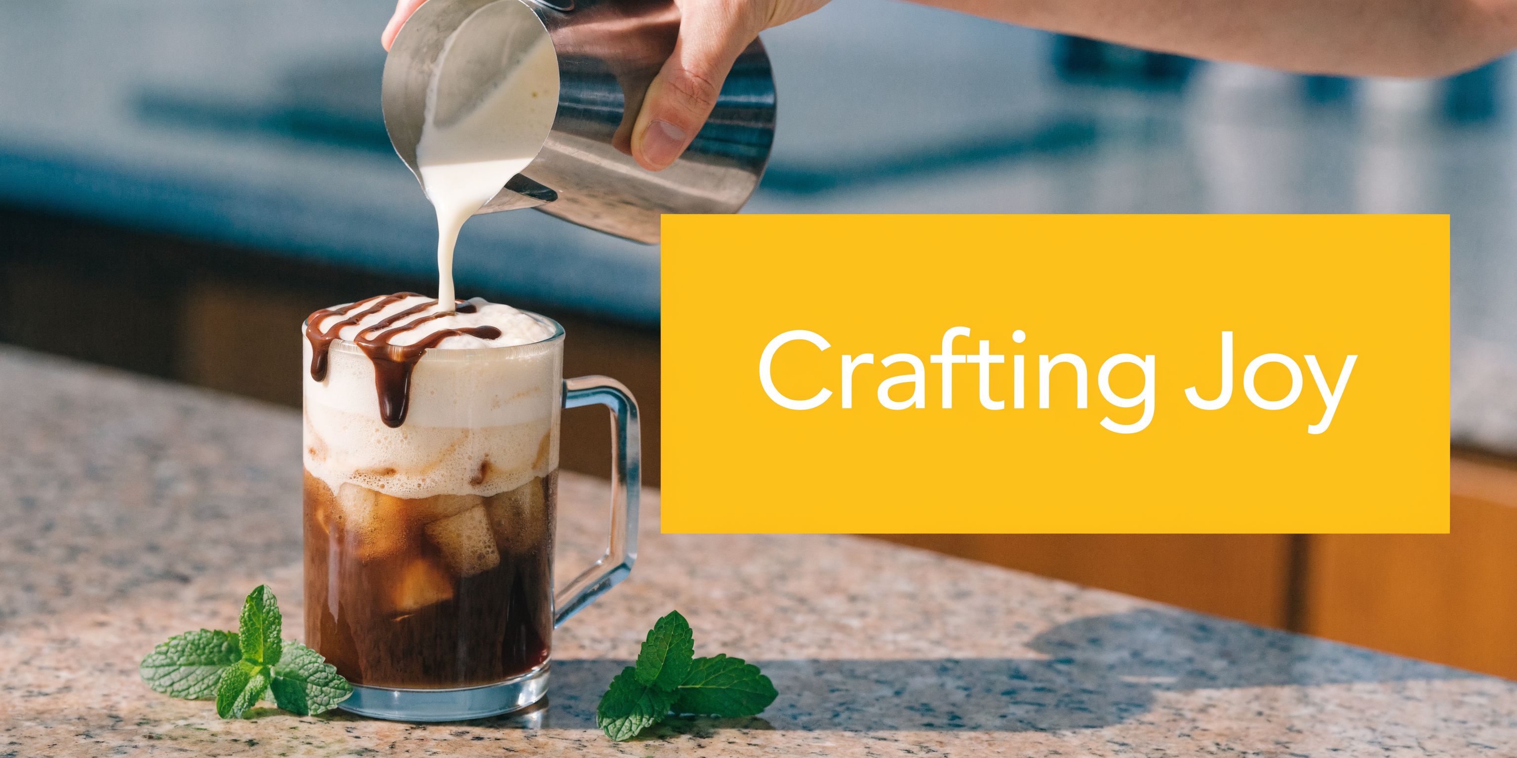 A hand pouring milk into a glass of iced peppermint mocha coffee decorated with chocolate drizzle